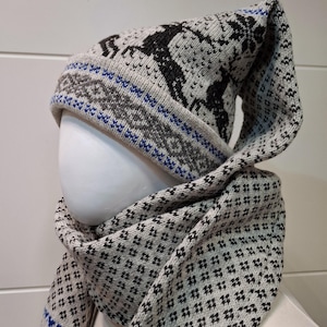 May include: A knitted hat and scarf set in light grey, black, and blue. The hat features a reindeer design and a long, pointed top. The scarf has a repeating diamond pattern. The set is displayed on a mannequin head.