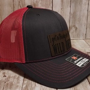 May include: A black and red trucker hat with a brown leather patch that says "I got a thing for wild ones".