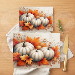 May include: Two rectangular art prints featuring white pumpkins and fall foliage. The pumpkins have dark stems and are surrounded by orange and yellow leaves. The prints are on a light background, evoking a harvest or autumn theme.