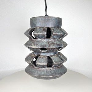 Peut inclure: Suspension en céramique grise et bleu-vert avec un design géométrique en couches et des formes découpées. Un cordon noir suspend la lampe au plafond. La lampe mesure environ 20 cm de haut.