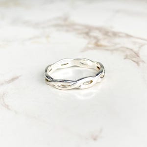Op de afbeelding: Een zilveren ring met een gevlochten ontwerp. De ring is simpel en elegant.