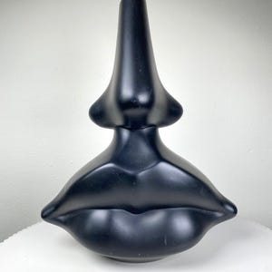 May include: A black ceramic vase shaped like a pair of lips with a nose on top.