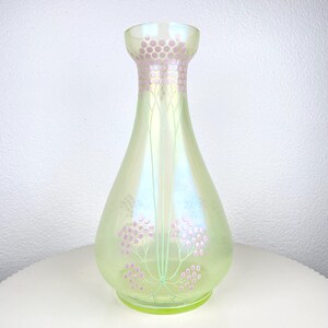May include: An iridescent glass vase in a pear shape, with a light green colour. It has a decorative pattern of pink floral designs and a matching pink dotted pattern around the neck. The vase is on a white surface.