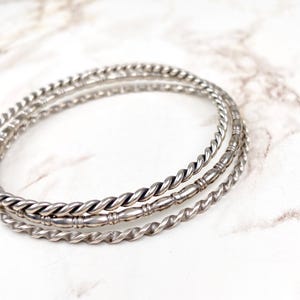 Op de afbeelding: Drie zilveren armbandjes, elk met een ander gedraaid ontwerp. De armbandjes zijn op elkaar gestapeld.