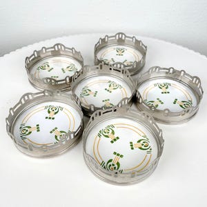 May include: Set of six vintage coasters with a silver-toned metal rim and a white center. The center features a green and gold geometric design. The coasters are arranged on a white surface.
