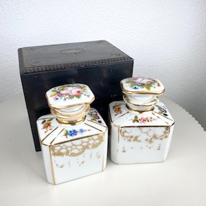 Op de afbeelding: Een set van drie keramische mokken met een gespikkelde, crèmekleurige glazuur. Elke mok heeft een handgeschilderd bloemmotief in blauw, groen en geel. De mokken hebben een eenvoudige, afgeronde vorm.
