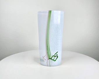Könnte beinhalten: Ein zylindrisches Glas mit weißer, strukturierter Oberfläche. Es hat vertikale grüne und rosa Linien sowie ein grünes, organisches Design in der Nähe des Bodens. Das Wort "BODA" ist auf der Seite sichtbar.