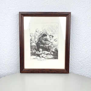 Puede incluir: Un grabado en blanco y negro enmarcado que representa a un grupo de personas, posiblemente una familia, en un estilo vintage detallado. El marco marrón oscuro rodea la obra de arte, que se encuentra sobre un fondo blanco.