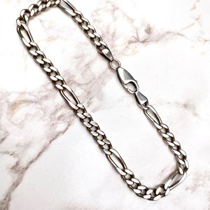 May include: A silver chain bracelet with a curb link design. The bracelet is made of a polished metal and has a lobster claw clasp.
