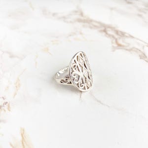 Puede incluir: Un anillo de plata con un diseño intrincado y calado. El anillo tiene forma ovalada y presenta un delicado patrón de filigrana.