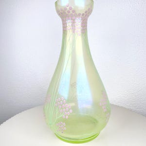 May include: A pearlescent green glass vase with a flared neck and a rounded body. The vase is decorated with pink floral patterns and delicate green stems. The vase is approximately 23 cm tall.