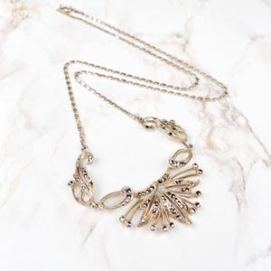 Può includere: Una collana d'argento con una catena delicata e un grande ciondolo ornato con pietre di marcasite. Il ciondolo presenta un design a forma di ventaglio con dettagli intricati.