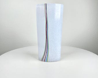Könnte beinhalten: Eine hohe, zylindrische Vase aus weißem Glas mit strukturierter Oberfläche. Ein vertikaler Streifen aus dünnen, farbigen Linien in Rot, Grün, Blau und Gelb verläuft die Seite hinunter. Die Vase steht auf einem weißen, runden Tisch.