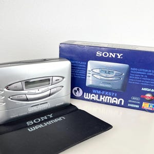 May include: Silver Sony Walkman WM-FX571 cassette player with a black carrying case. The box shows the Walkman and has the text "MEGA BASS" and "GROOVE". The Walkman has a digital display and control buttons.
