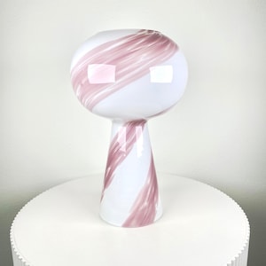 Op de afbeelding: Een witte keramische vaas met een roze en witte swirl-design. De vaas heeft een ronde bovenkant en een hoge, smalle voet.