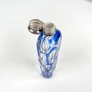 May include: A blue glass perfume bottle with a silver lid. The bottle has a cut glass design with a floral pattern. The lid is open, revealing the bottle's opening. The bottle is approximately 4 inches tall.