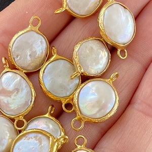 May include: A close-up of a group of gold-toned metal charms with white pearl inlays. The charms have a loop at the top for attaching to jewellery.