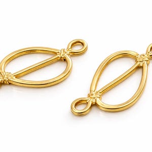 Puede incluir: Dos cierres de joyería de metal dorado. Cada cierre presenta un diseño ovalado con una barra horizontal en el centro y extremos en bucle. Los cierres se muestran sobre un fondo blanco.