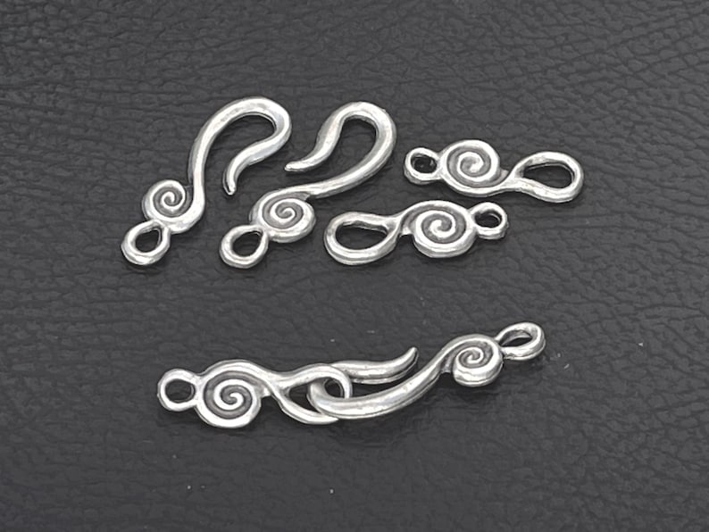 May include: A collection of silver-toned metal jewelry clasps featuring a spiral design. The set includes two S-shaped hook components and two matching loop components, with one pair shown connected together to demonstrate the functional closure mechanism.