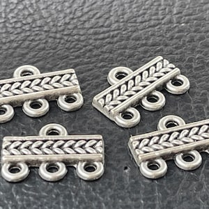 May include: Four silver-toned metal connector pieces with a braided design and three loops each. The connectors are designed for jewelry making.