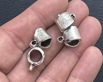 Może przedstawiać: Trzy małe, srebrne metalowe zawieszki w kształcie miniaturowych kubków lub filiżanek. Każda zawieszka ma teksturowane, rustykalne wykończenie z małym kółeczkiem z boku do zawieszenia, ukazując puste wnętrze oraz zaokrąglony uchwyt.