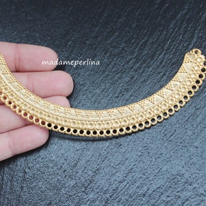 Puede incluir: Pendiente de collar de metal dorado con un diseño decorativo. El pendiente tiene forma de media luna y tiene un borde festoneado.