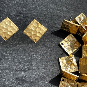May include: A close-up of gold-toned square earring blanks with a hammered texture. The earring blanks have a hole for attaching earring posts. There are multiple earring blanks in the image.