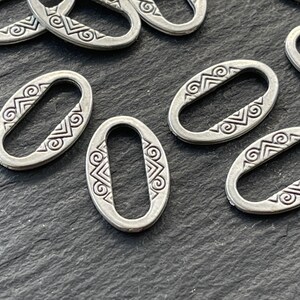 May include: Silver oval-shaped metal rings with a decorative design. The rings have a smooth, polished finish and a slightly raised design.