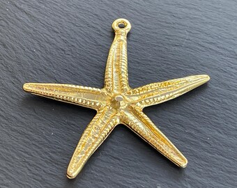 May include: A gold-coloured starfish charm with five points and a textured surface. The charm has a small loop at the top for attaching to a necklace or bracelet. The starfish is a decorative element.