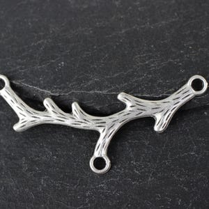Può includere: Ciondolo a forma di ramo in metallo color argento con tre anelli a salto. Il ramo ha una superficie testurizzata che ricorda la corteccia.