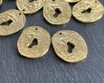 May include: A collection of small, round, gold-coloured metal charms with a textured, hammered surface. Each charm features an irregular, keyhole-shaped cutout in the centre and a single small circular hole at the top for attachment purposes.