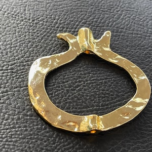 May include: A gold-colored metal pomegranate-shaped ring holder. The ring holder is smooth and has a slightly textured surface.