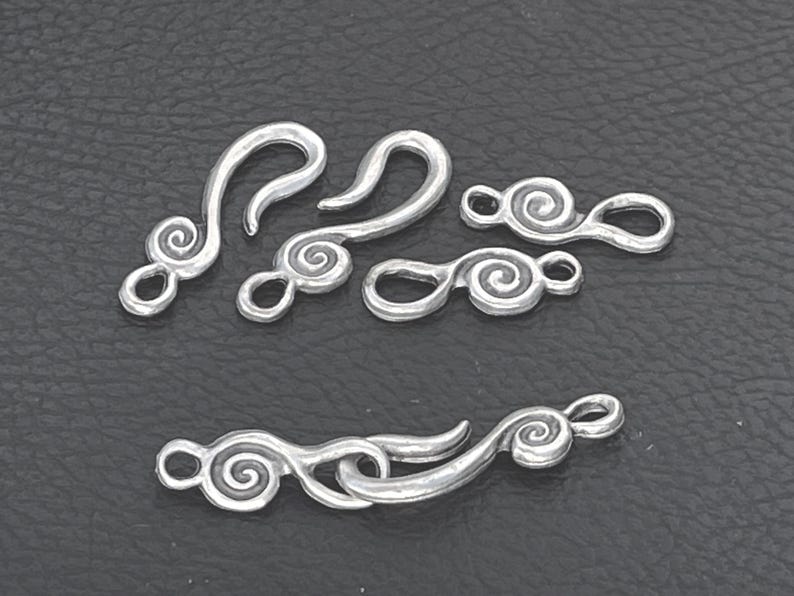 May include: A collection of silver-toned metal jewelry clasps featuring a decorative spiral design. The set includes several hook-and-eye style components, with some pieces shown separated and one pair connected together to demonstrate the mechanism.