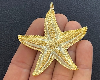 May include: A gold-toned starfish pendant featuring a highly textured, bumpy surface and a small loop at the top for attachment. The five-pointed sea creature design has a metallic finish with raised details across its entire front surface.