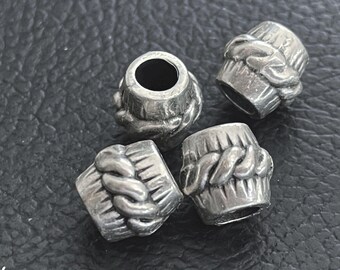 May include: Four silver-toned metal beads with a cylindrical shape, featuring a central raised twisted rope pattern and vertical grooved lines on the top and bottom sections. Each bead has a hollow center hole for threading onto a cord or chain.