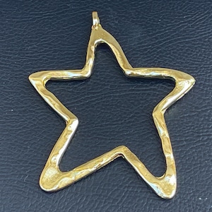 May include: A gold-colored metal star-shaped pendant with a hammered texture. The star is open and has a loop at the top for attaching to a chain.