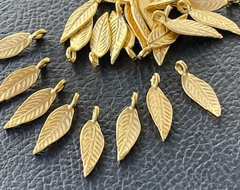 May include: A collection of small, gold-colored metal leaf charms, each featuring a detailed vein pattern and a small circular loop at the top for attachment. The charms are arranged in a loose cluster and a semi-circular formation.
