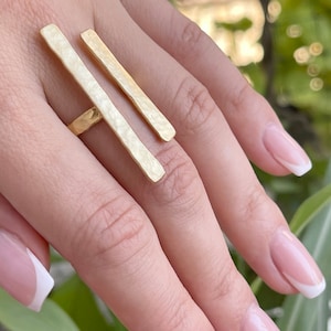 May include: Gold-toned double bar ring with a hammered finish. The ring is worn on the index finger of a hand.
