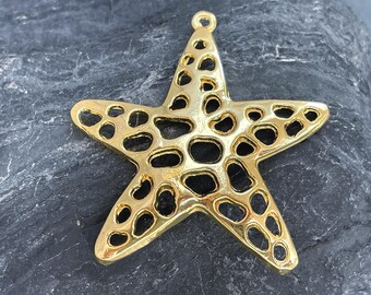May include: A gold-toned metal starfish pendant featuring an intricate openwork design with irregular, rounded cutouts throughout its five-pointed structure and a small circular loop at the top for attachment to a chain or cord.