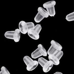 Peut inclure: Gros plan sur un groupe de dos d'oreille en plastique transparent. Les dos sont petits et de forme arrondie. Ils sont conçus pour être utilisés avec des boucles d'oreilles à clous.