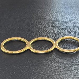 May include: A triple ring set in gold tone, featuring three connected circles. The rings are smooth and shiny.