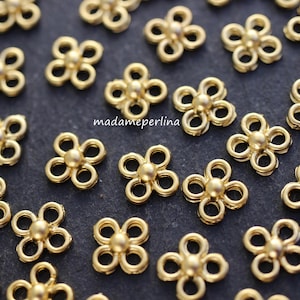 May include: A collection of gold-toned metal flower-shaped connectors. The connectors have a four-petal design with a small bead in the center of each petal.