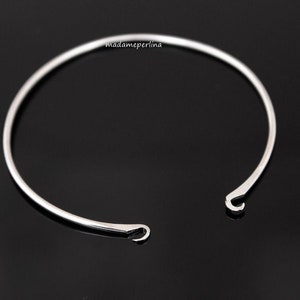 May include: A silver bangle bracelet with two open hooks on the side.