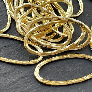 May include: Close-up of several gold-colored oval-shaped jewelry findings. The findings have a hammered texture and are scattered on a dark surface. The oval shapes vary in size and are made of metal.