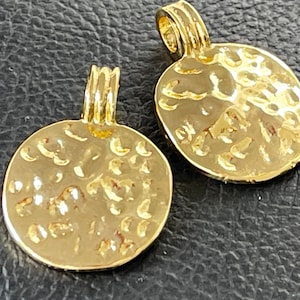 Könnte beinhalten: Zwei goldfarbene Metall-Anhänger mit gehämmerter Textur und einer Öse oben zum Anbringen an Schmuck.