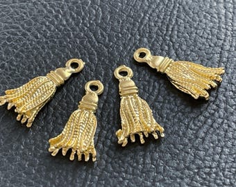 Könnte beinhalten: Drei goldfarbene Metallanhänger in Form von Quasten. Jeder Anhänger verfügt über eine kleine kreisförmige Öse an der Oberseite zur Befestigung, einen gerippten zylindrischen Hals und eine ausgestellte, texturierte Basis, die hängende Fäden imitiert.