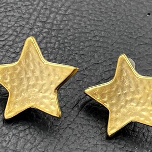May include: A pair of gold star-shaped earrings. The stars have a textured surface.