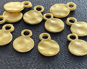 May include: Ten gold-colored metal charms with a round, textured surface and a loop at the top. The charms are scattered on a dark surface.