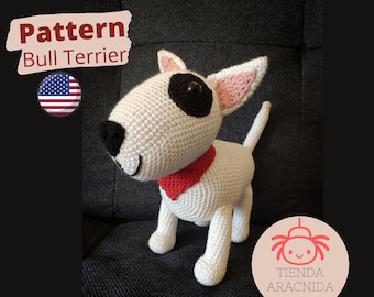 May include: A white crocheted amigurumi bull terrier with black eyes and a red collar. The crocheted toy is sitting on a gray couch. The image includes the text "Pattern Bull Terrier" and a US flag.
