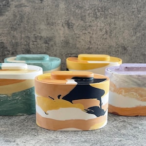 May include: Five oval-shaped containers with lids. The containers are made of a marbled material with different color combinations, including green, yellow, black, white, and purple.